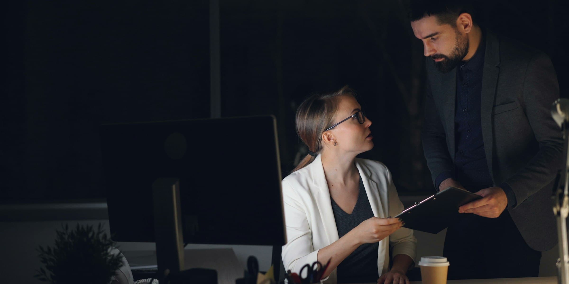 A product manager reviewing notes with a colleague at a late-night desk